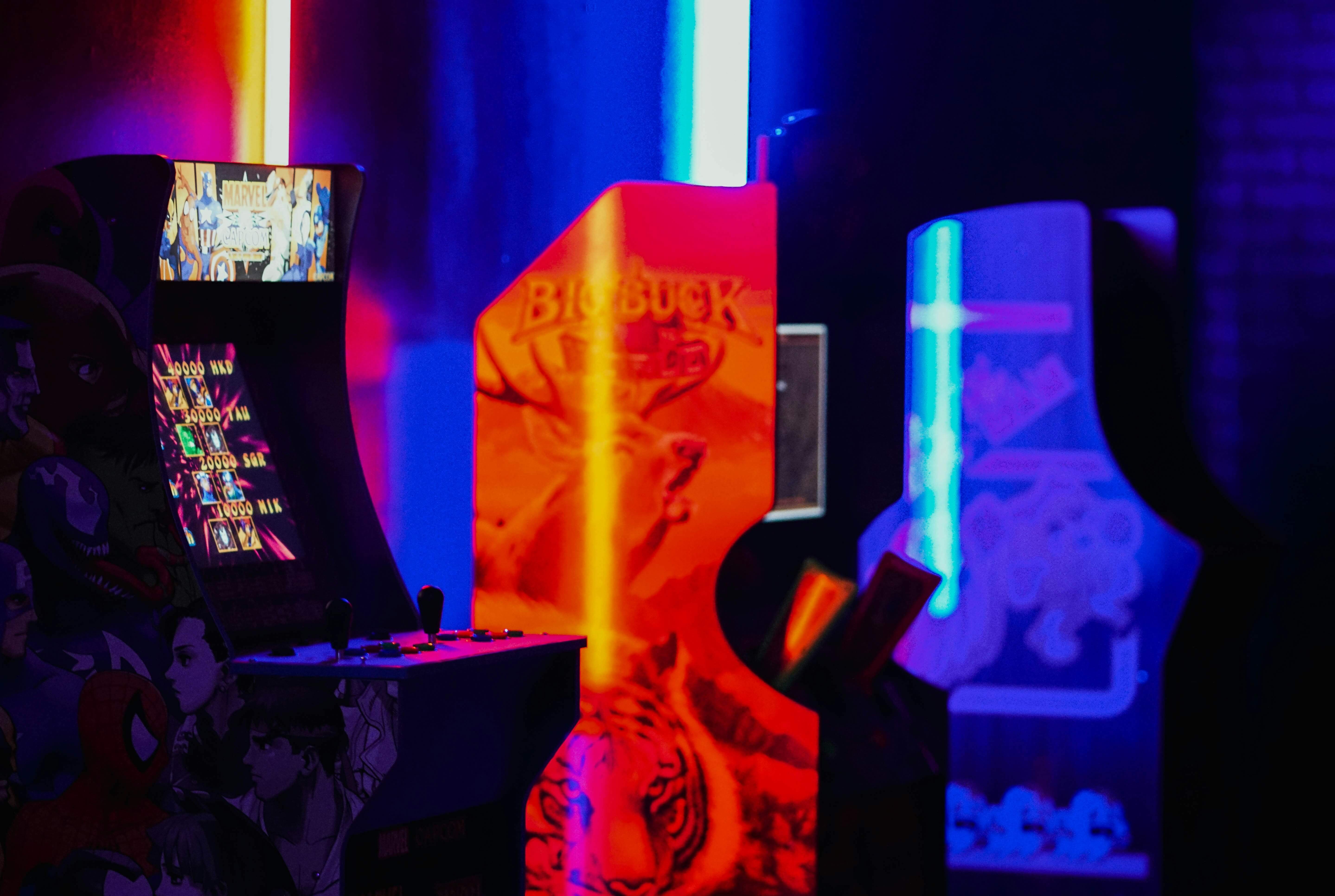 a photo of 3 arcade cabnets lit by various bright neon red and blue lights