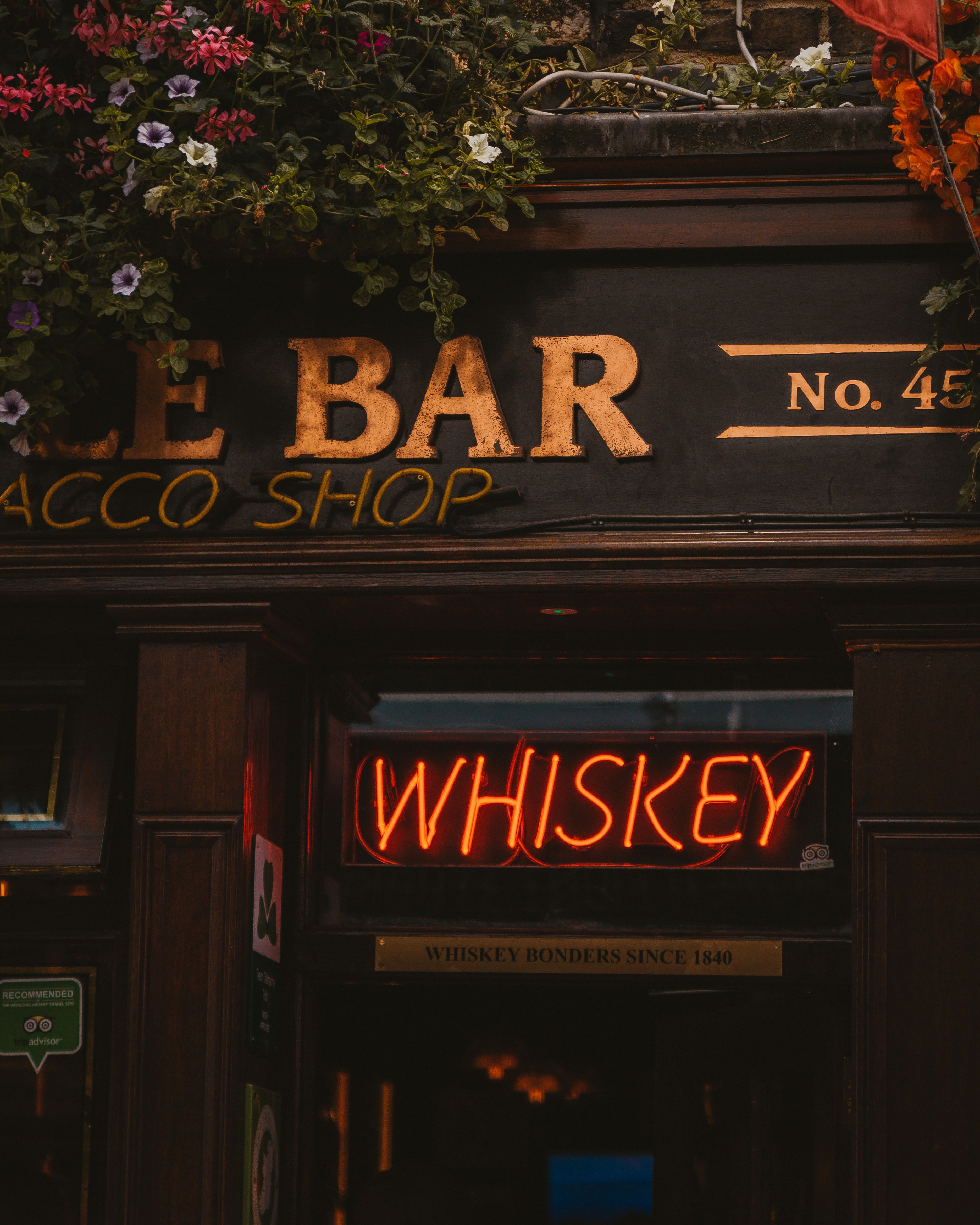 a photo of a portion of a bar and tabacoo shop with a orange neon sign in the window reading whiskey